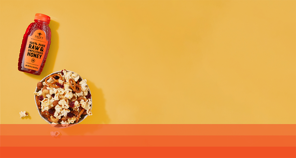 Bowl of popcorn next to bottle of honey.