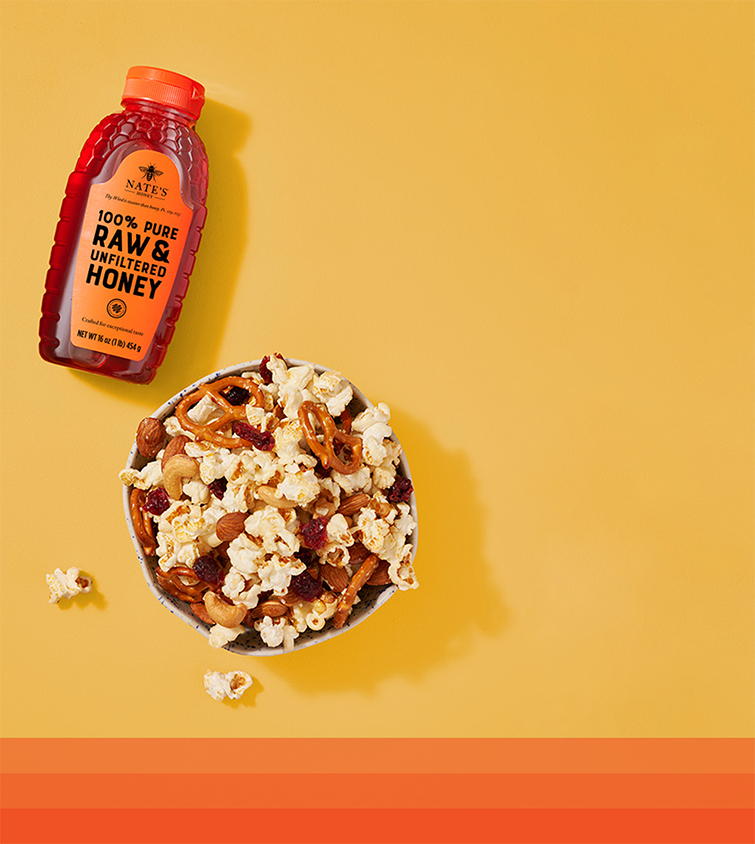 Bowl of popcorn next to bottle of honey.