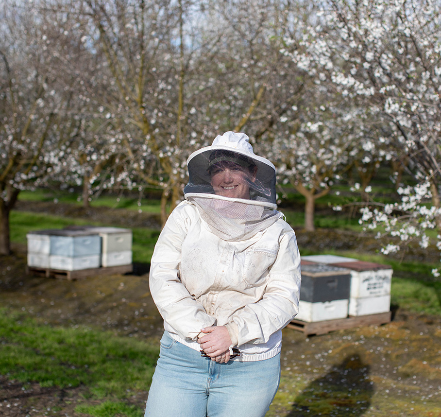 Beekeeper in protective suit near hives in orchard